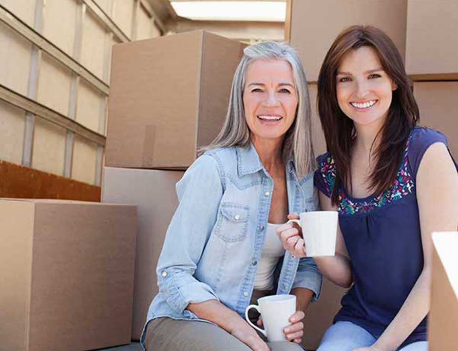 Two women sitting together with cups of tea among packing boxes during a house clearance